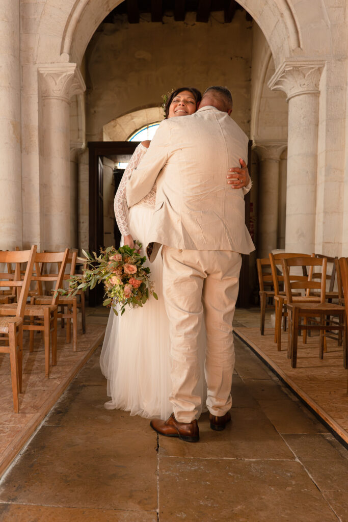 Les mariés s'enlaçant dans une église pendant la séance couple. On peut voir la marié riant de face et le marié de dos la prenant dans ses bras