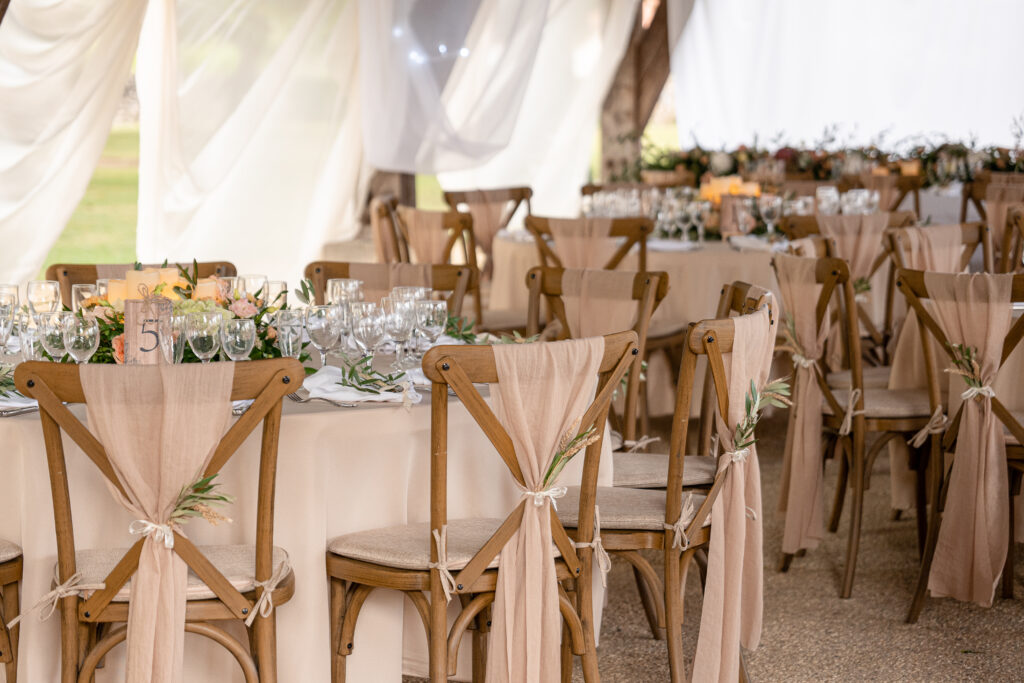 Photographie d'un plan global d'une salle décorée dans des tons beiges pastel avec une décoration élégante sur les chaises et des rameaux d'olivier disposé sur les tables