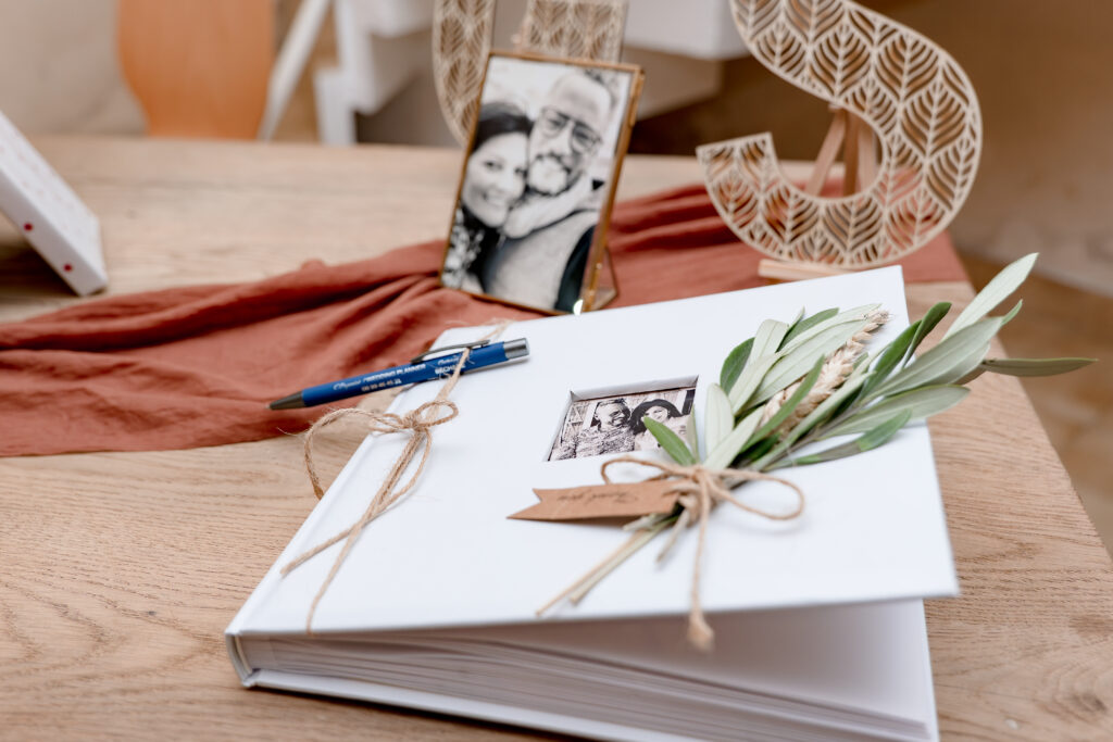 Gros plan sur un carnet déposé sur une table avec un stylo et un cadre photo des mariés en arrière plan