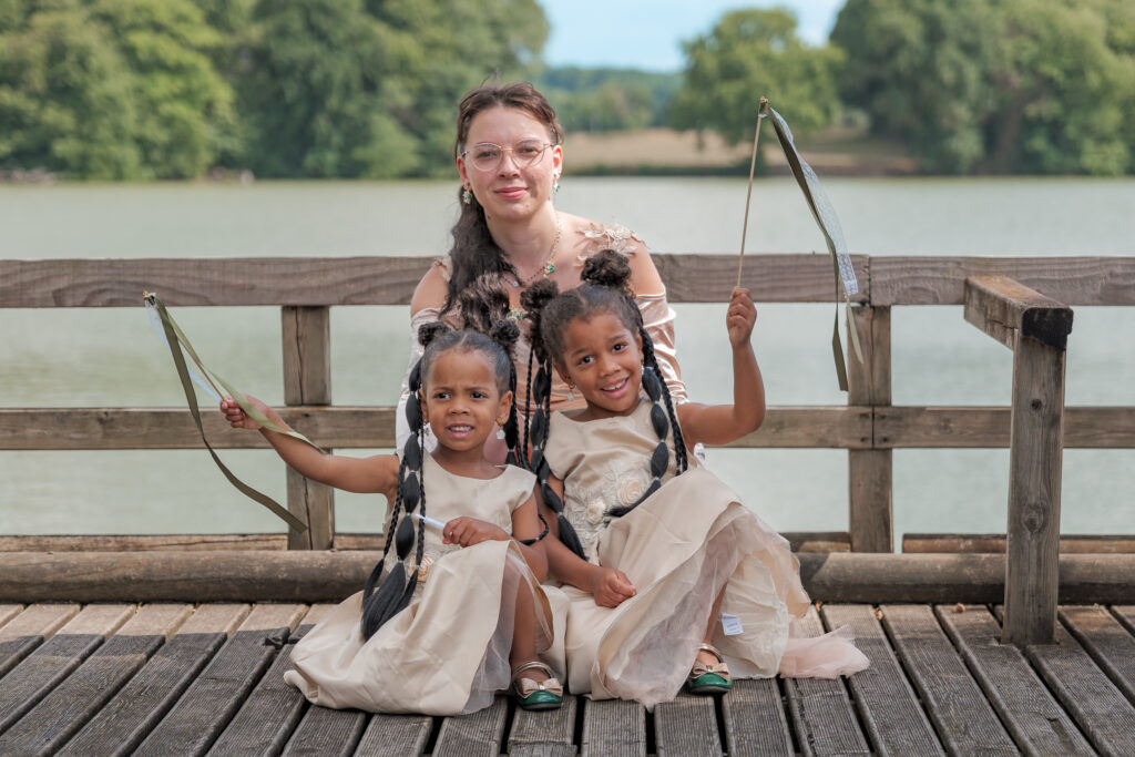 Une mère pose avec ses deux petites filles devant un bel étang sur un ponton par une journée ensoleillée