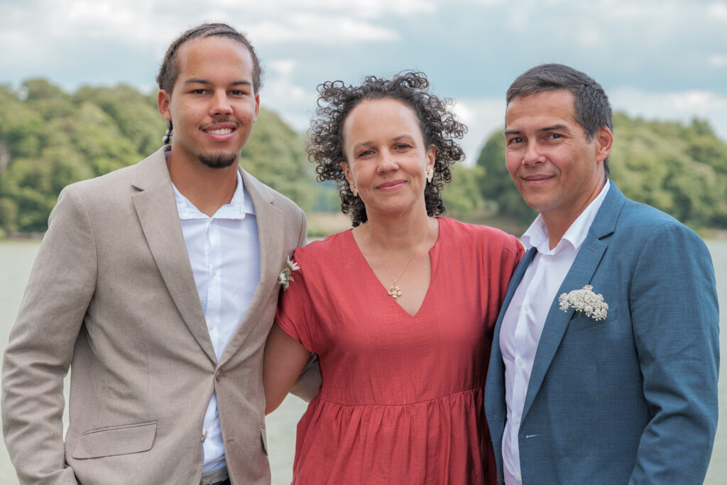 Photo de groupe lors du vin d'honneur mettant en avant au centre une femme vêtue d'une robe rouge, un jeune homme à gauche et son mari à droite