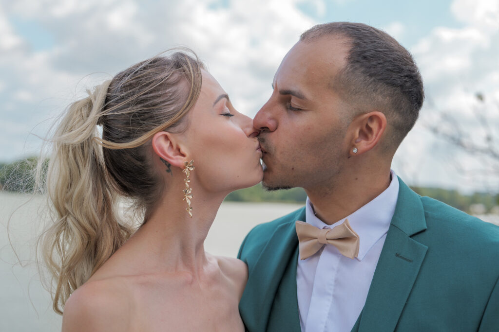 Couple s'embrassant pendant les photos de groupe lors d'un vin d'honneur. Nous pouvons voir en arrière plan l'étang de la Cazine de Noth.