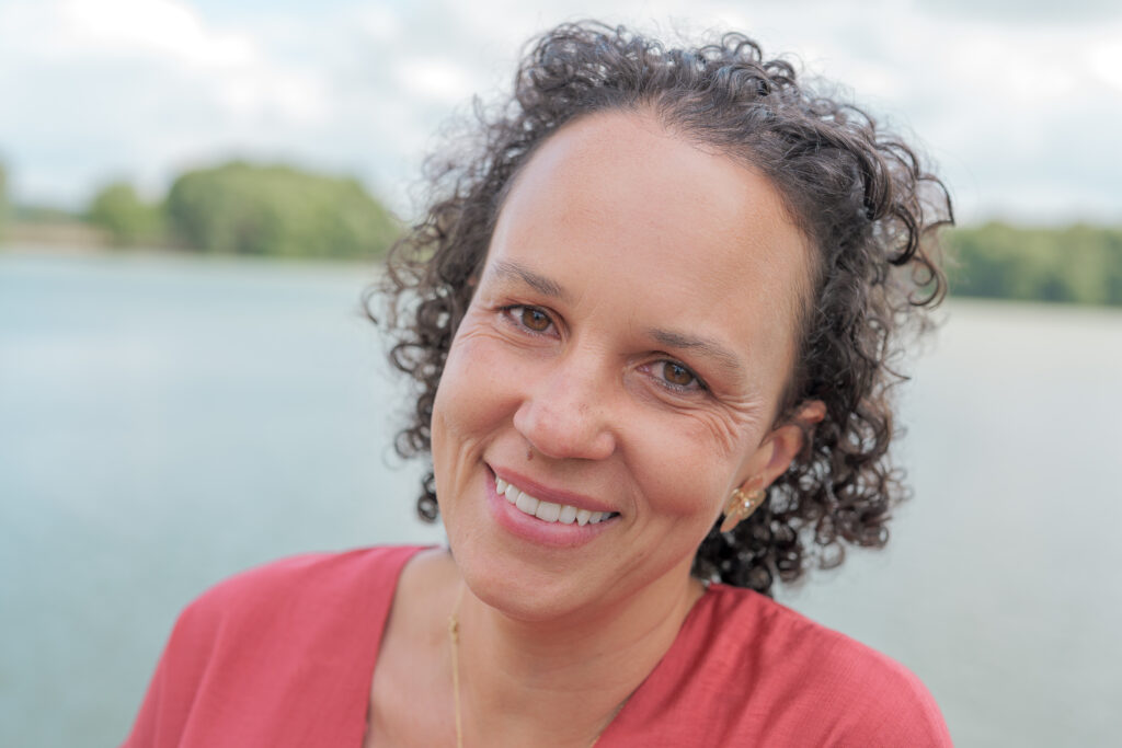 Invitée de mariage souriant à l'objectif avec en arrière plan un étang  et des arbres au loin