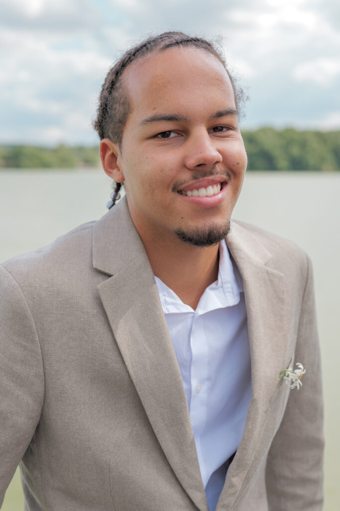 Jeune invité de mariage et souriant à l'objectif avec en arrière plan un étang  et des arbres au loin