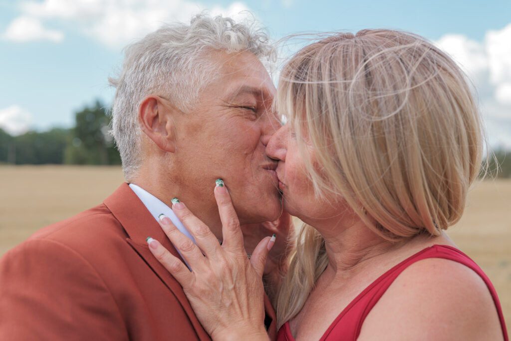 Parents du marié s'embrassant lors de la séance des photos de groupe avec en arrière plan un champs de blé grillé par le soleil