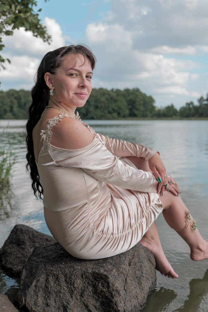 Portrait d'une jeune femme assise sur un rocher au bord de l'eau et habillé d'une jolie robe champagne