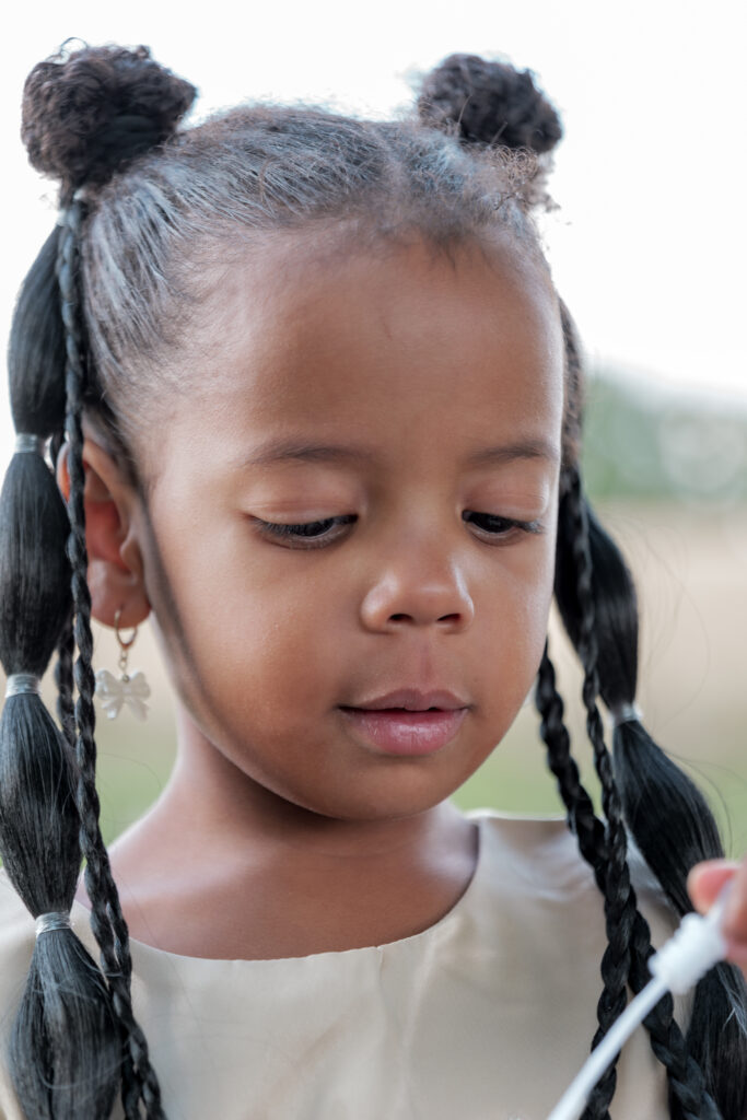 Portrait d'une petite fille regardant vers son jouet et portant de jolies tresses