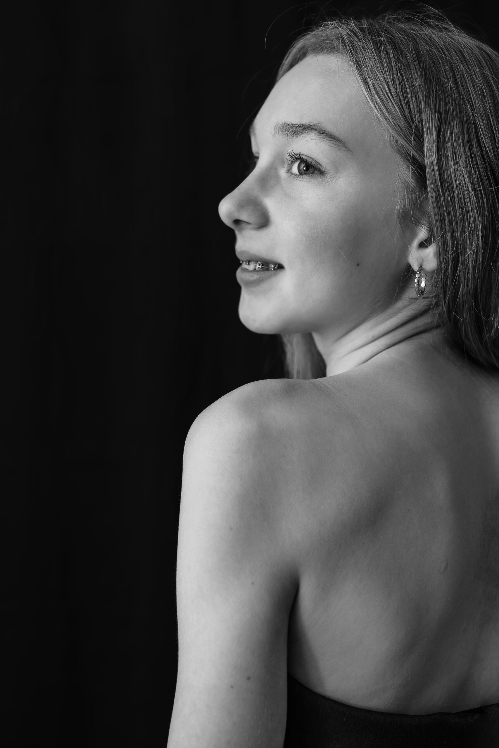 Portrait de dos en noir et blanc d'une jeune fille le visage de profil et le regard tourné vers la gauche, mettant en avant son épaule dégagée
