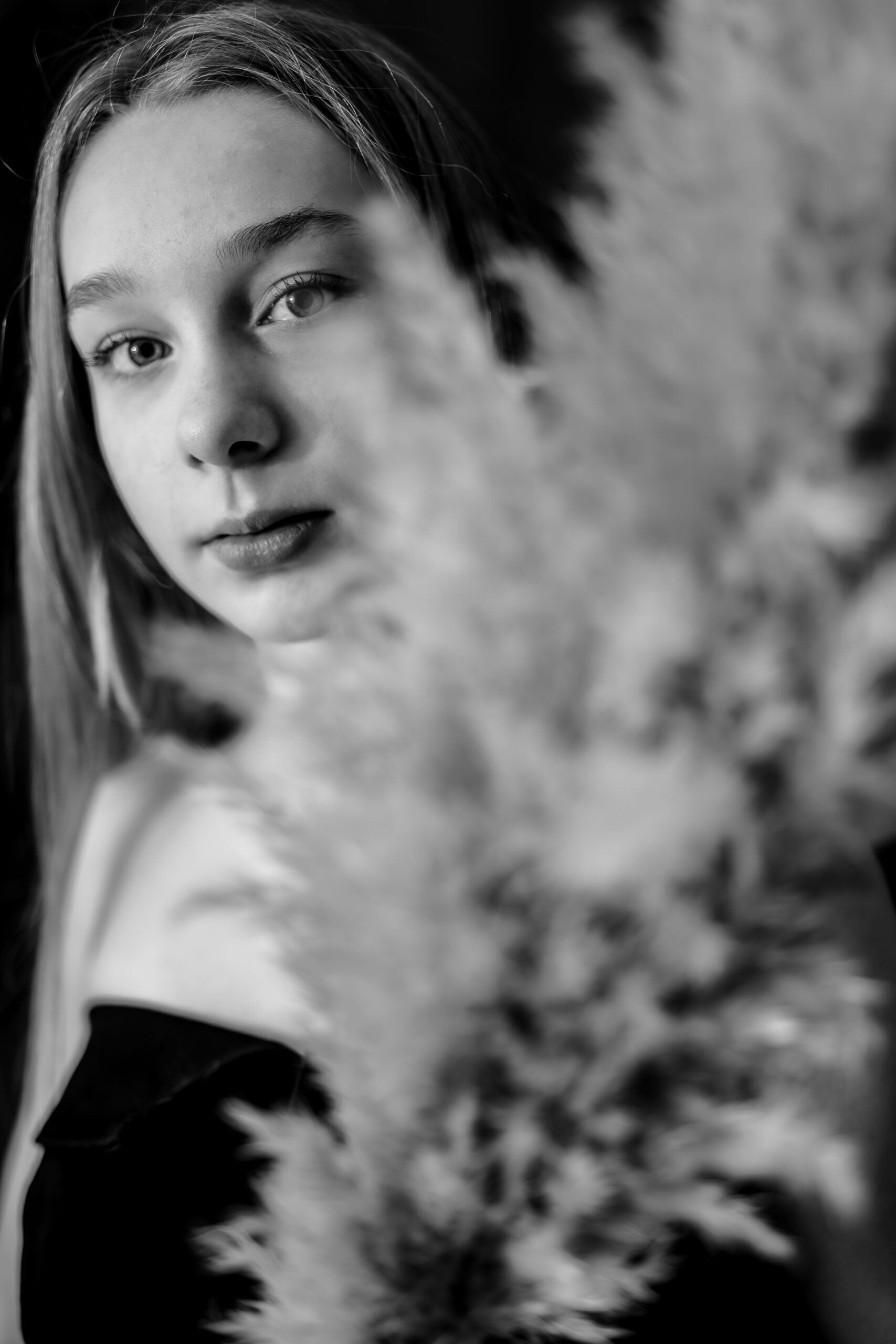 Portrait artistique en noir et blanc d'une jeune fille à demi cachée derrière une fleur de pampa en flou de premier plan