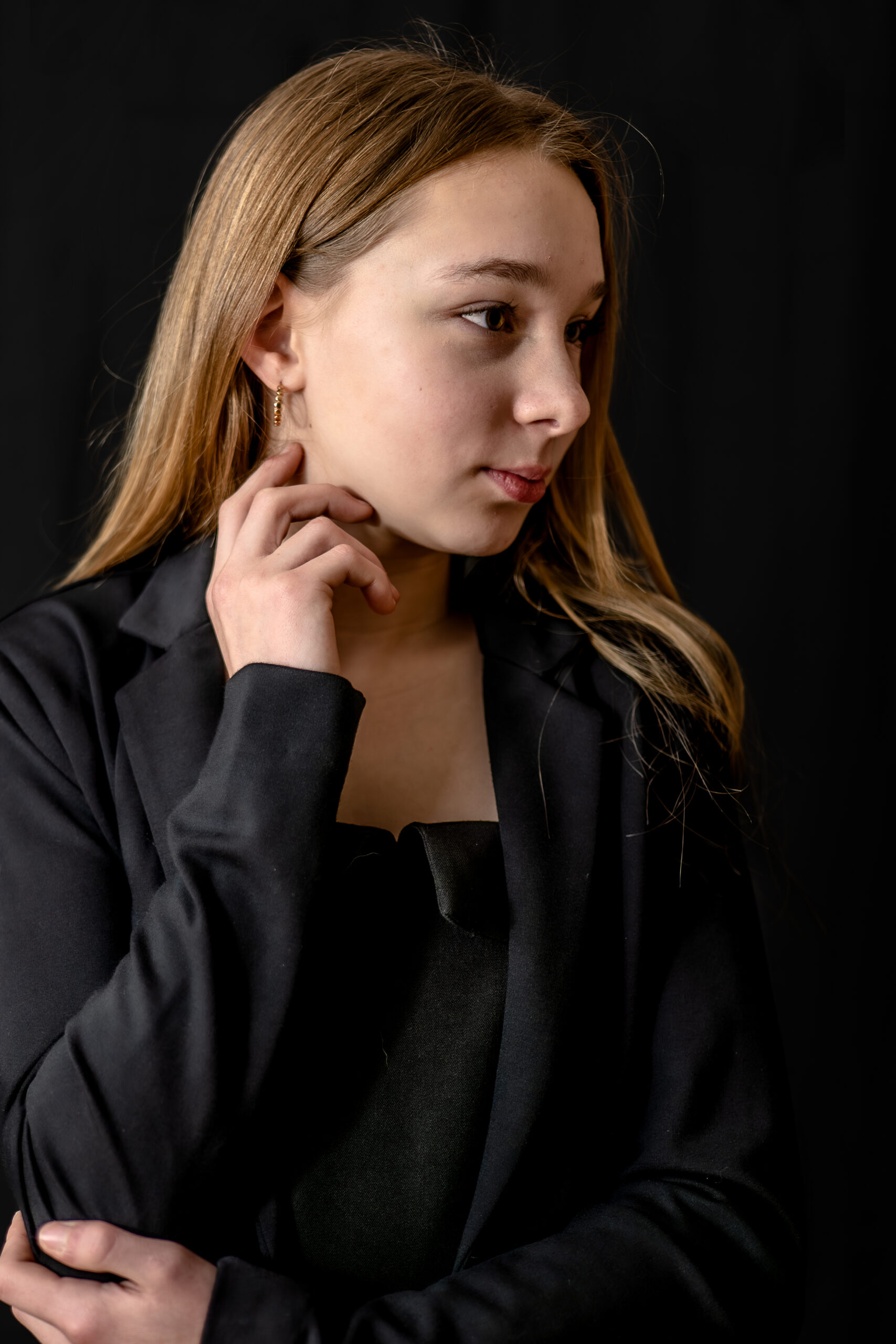 Pland de 3/4 d'une jeune fille sur fond noir posant avec une main près de l'oreille