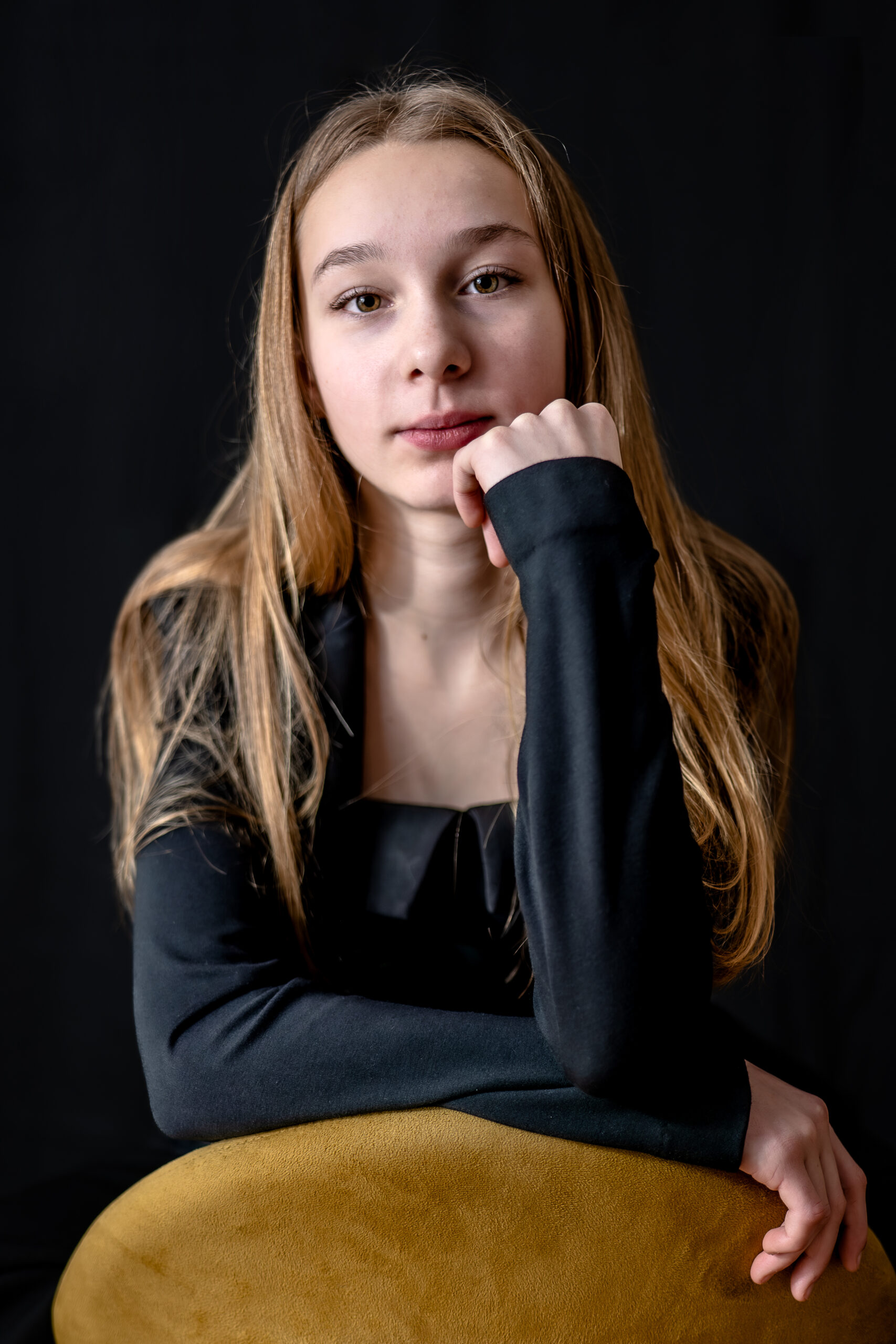 Plan de face d'une jeune fille avec une veste noir et accoudée le dossier d'une chaise