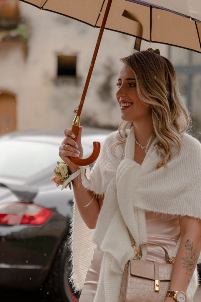 Portrait éloigné de la fille du marié tenant un parapluie et habillé d'un d'une écharpe blanche couvrant ses épaules. On peut voir une voiture noir en arrière plan