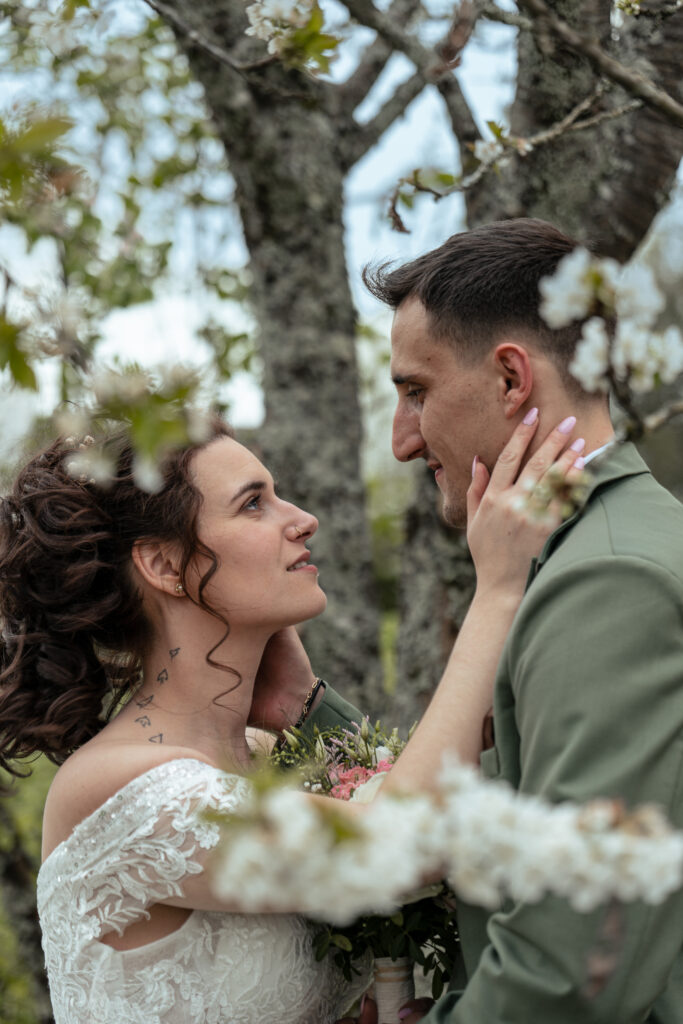 Flou de premier plan sur des cerisiers blancs en fleurs et regard intense des mariés à travers les branches de l'arbre