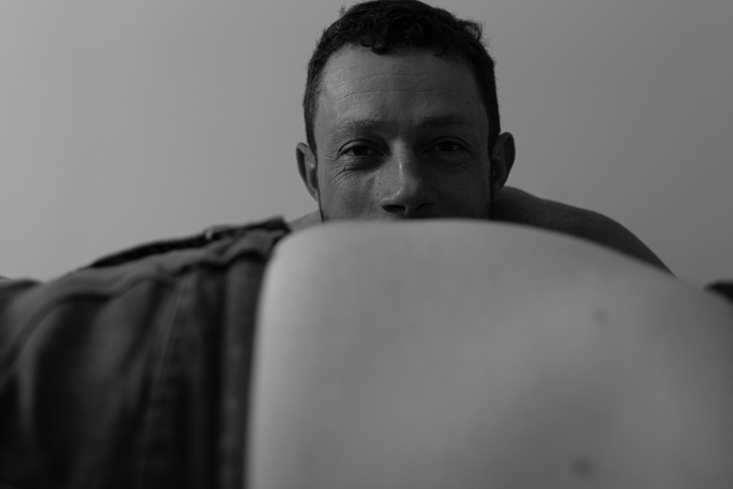 Portrait en noir et blanc d'un futur papa à demi caché derrière le ventre de la future maman en flou de premier plan