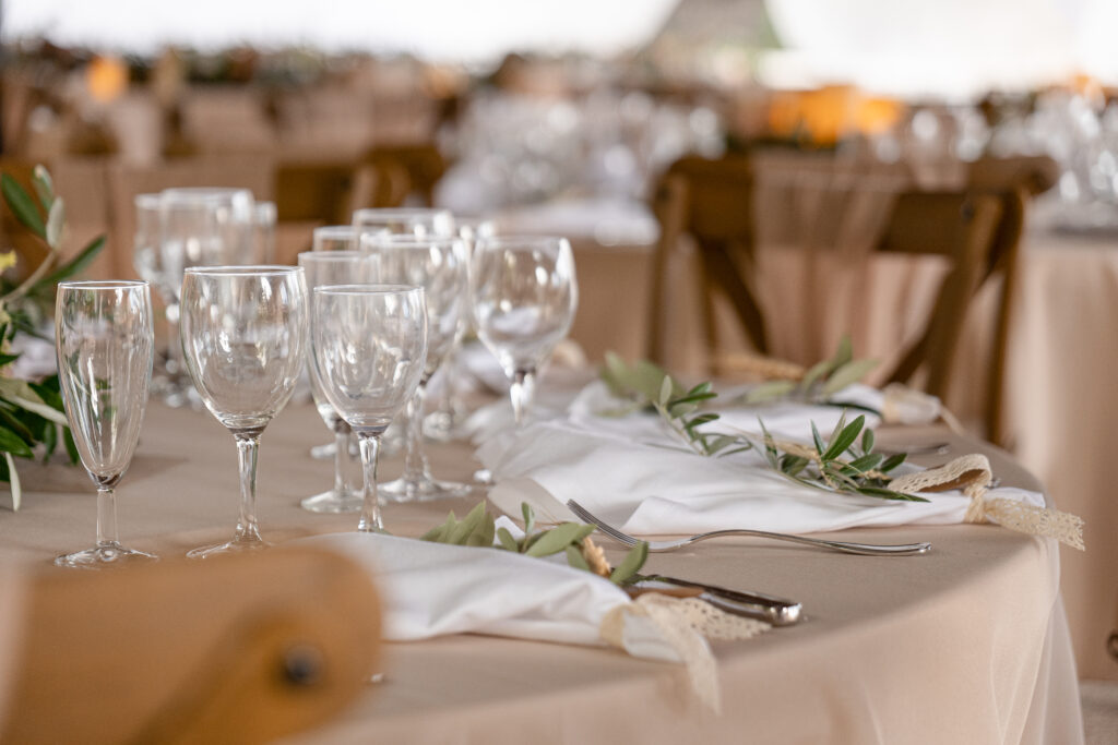 Plan rapproché sur la décoration de salle en plein air où l'on peut voir des rameaux d'olivier disposés sur les tables dans une ambiance beige élégante
