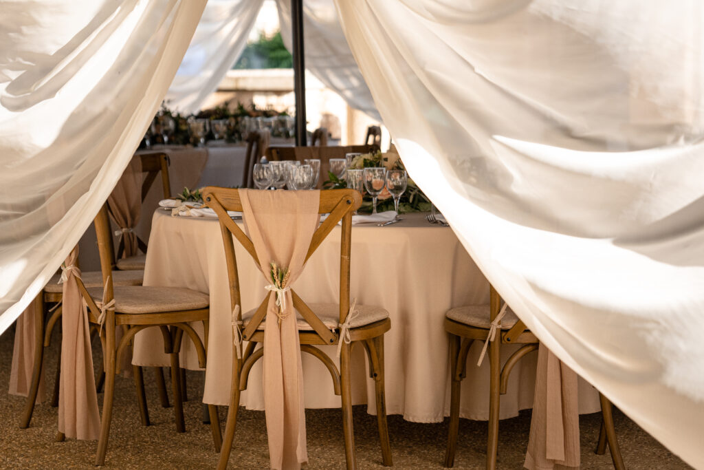 Décoration extérieur de mariage avec un plan sur une chaise arborant un noeud en voilage. Des rideaux retombant de part et d'autre laissant voir la disposition des tables