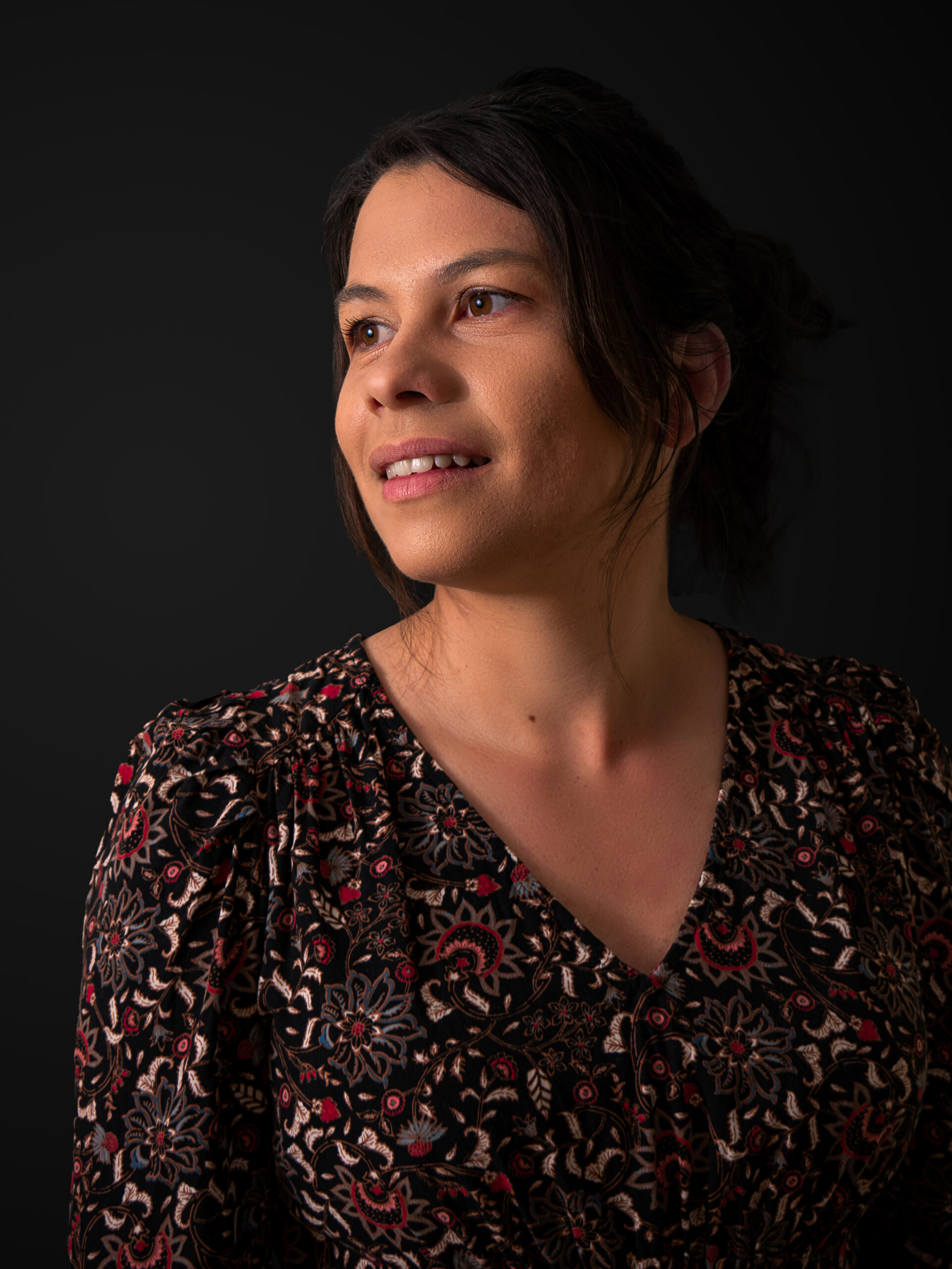 Portrait buste de 3/4 face, visage et regard tourné vers la gauche et sur fond noir avec un doux sourire