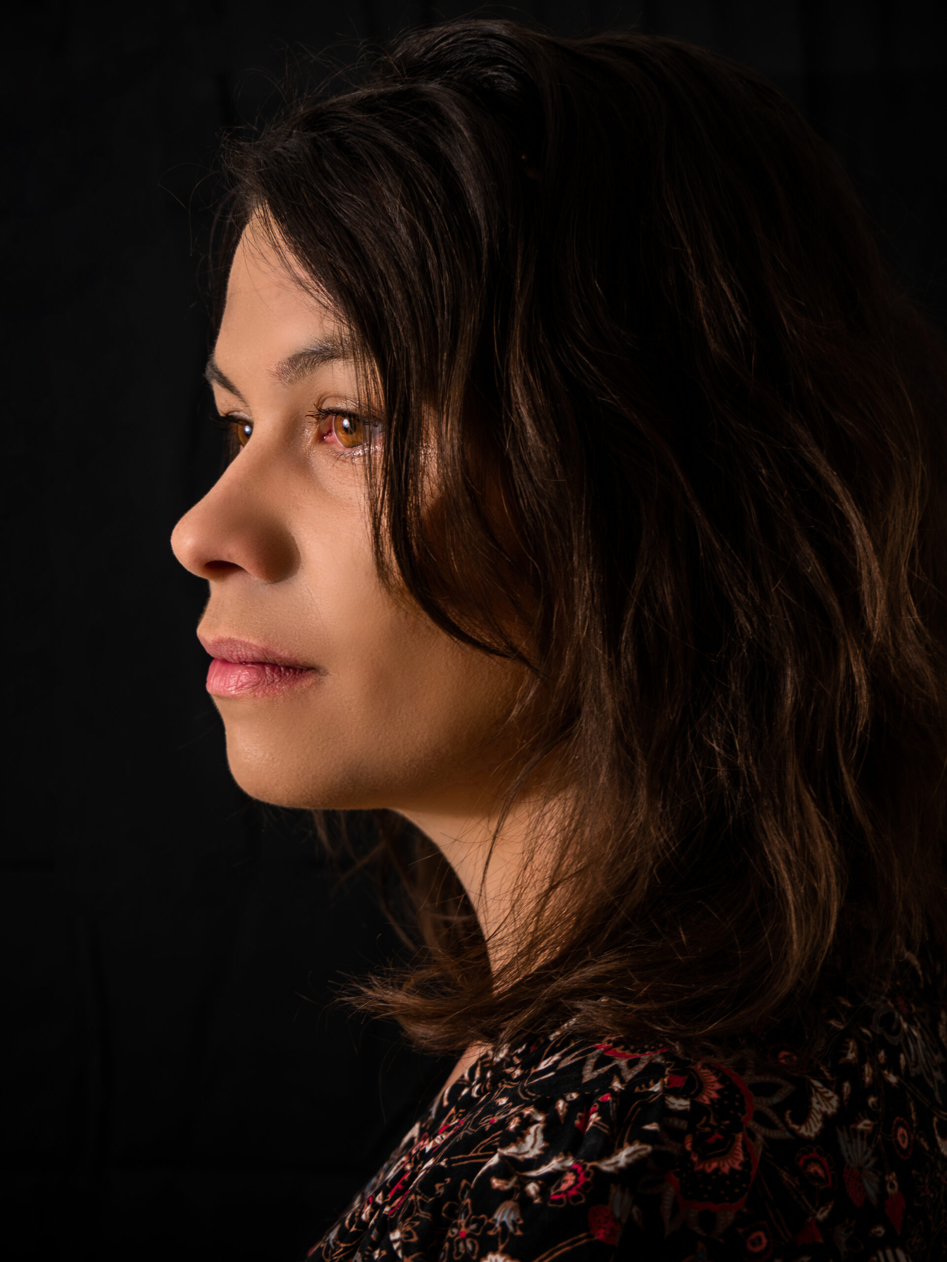 Portrait artistique d'une jeune femme dans un demi profil sur fond noir le regard porté vers la gauche au loin
