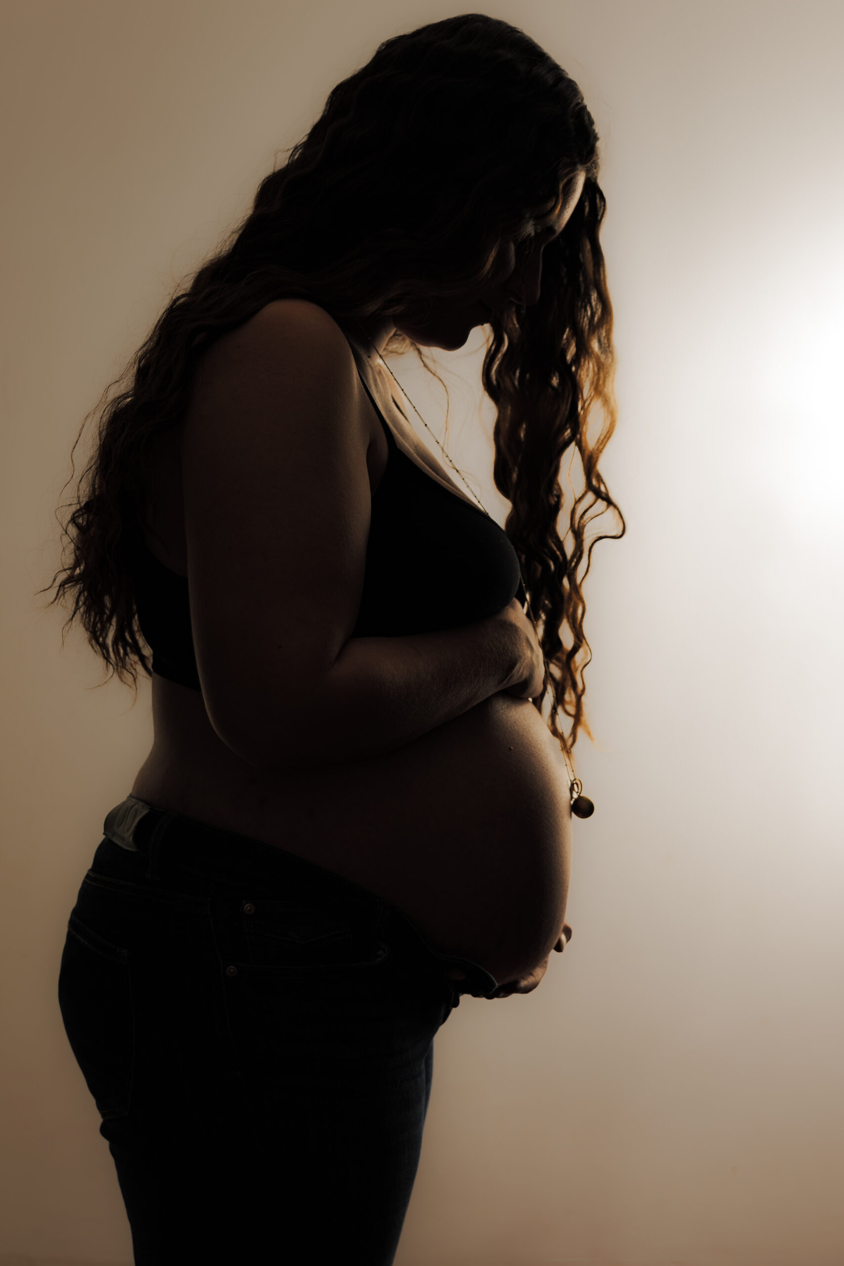Portrait en plan taille dans des teintes sombres d'une future mère de profil les cheveux descendant en cascade