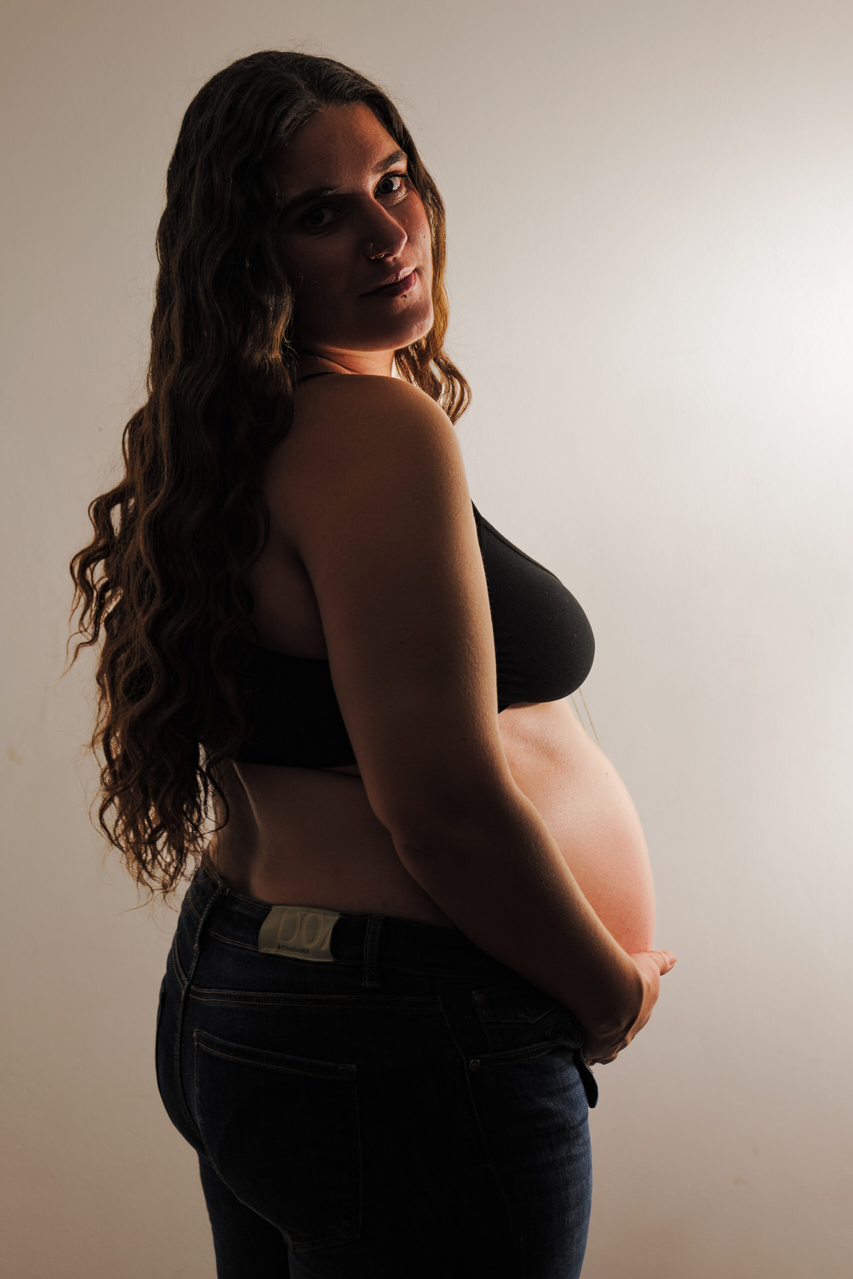 Portrait en plan taille dans des teintes chaudes d'une future mère regardant l'objectif de 3/4 dos