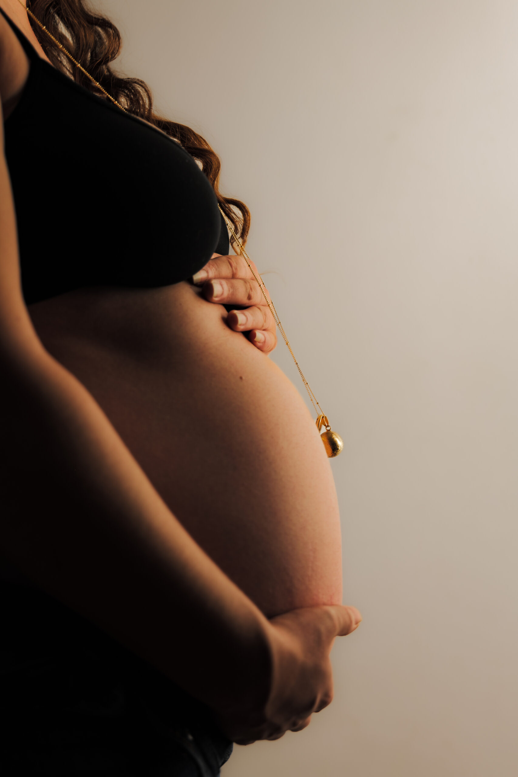 Plan rapproché dans des teintes dorées du ventre d'une future mère mettant en valeur un bola en or 