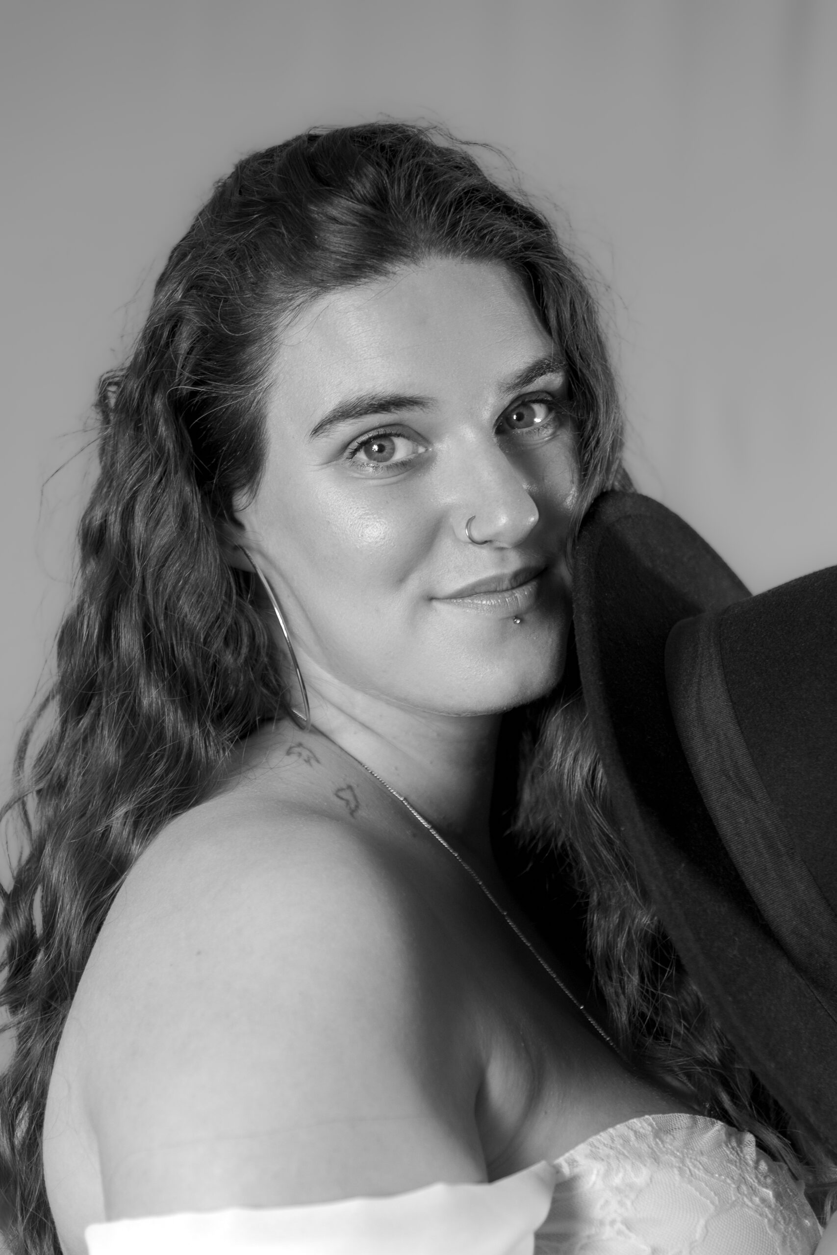 Portrait en noir et blanc d'une femme cachant un peu de son visage derrière un chapeau le regard face à l'objectif et avec un sourire doux