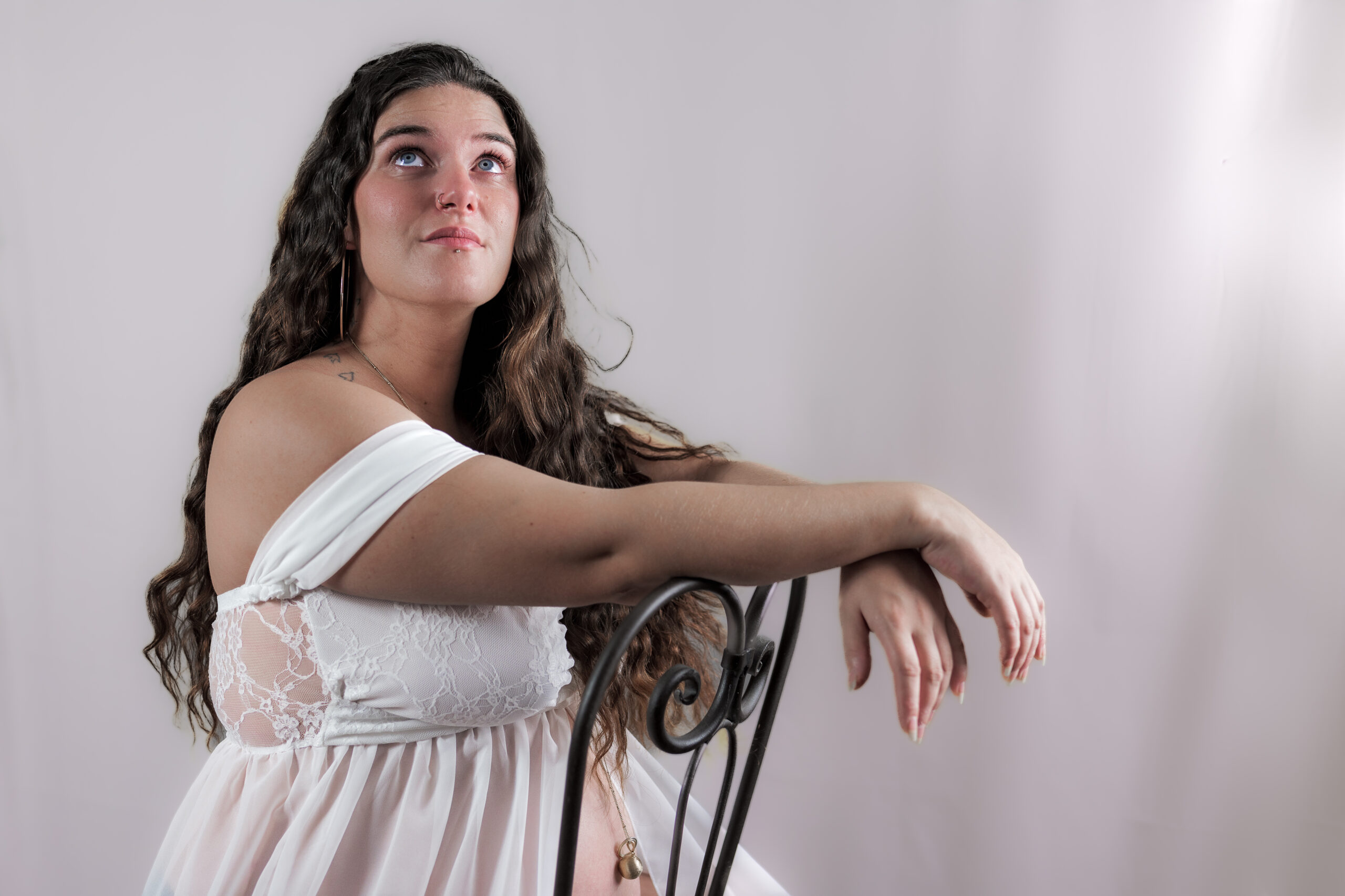 Portrait d'une femme enceinte assise à califourchon sur une chaise avec un éclairage doux et un fond rosé