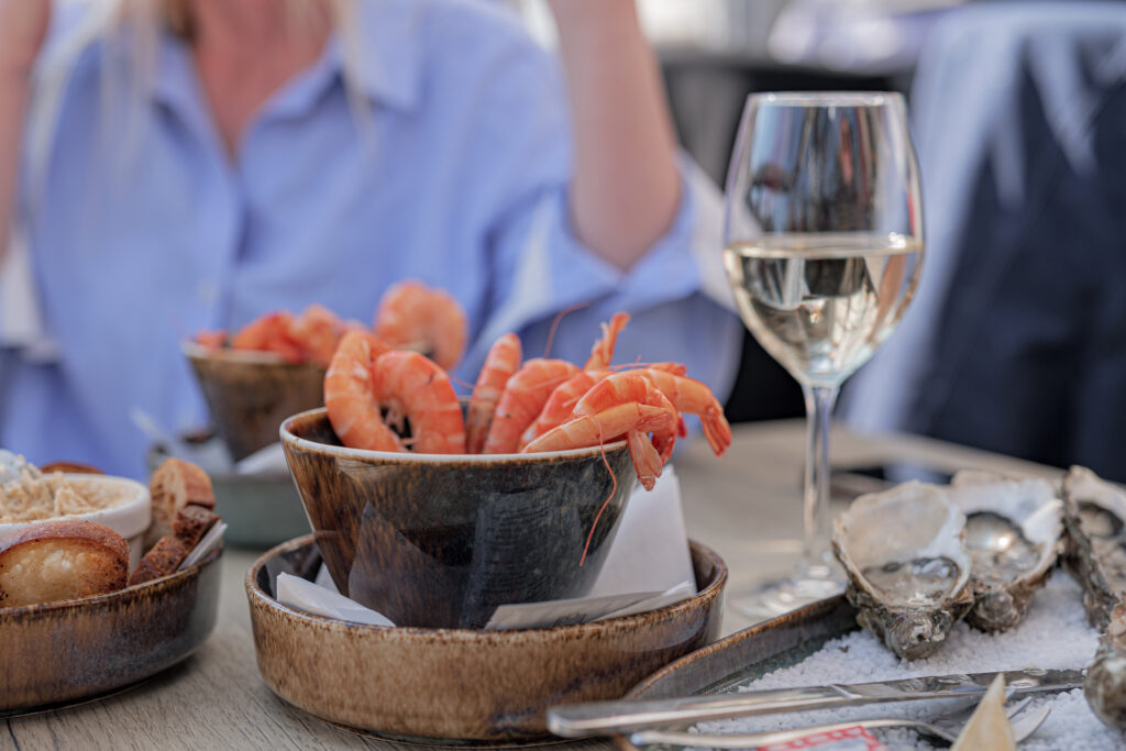 Image d'un repas partagé à une terrasse de restaurant à l'île de ré représentant des crevettes un plateau d'huîtres et un verre de vin blanc.