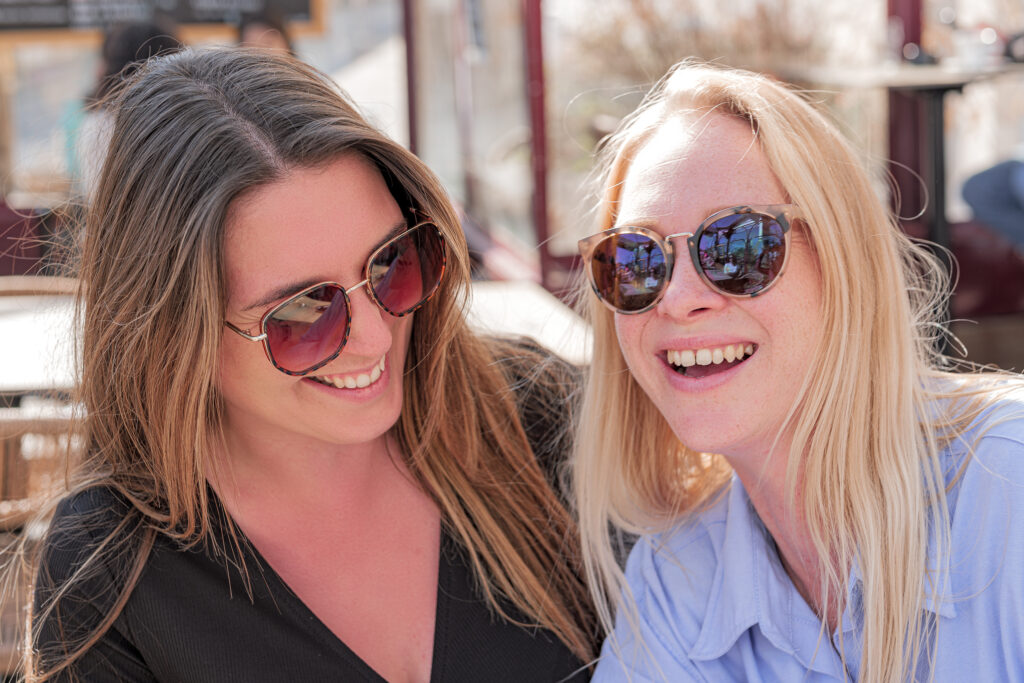 Photographie de deux amies riant à la terrasse d'un café au soleil pendant une belle journée