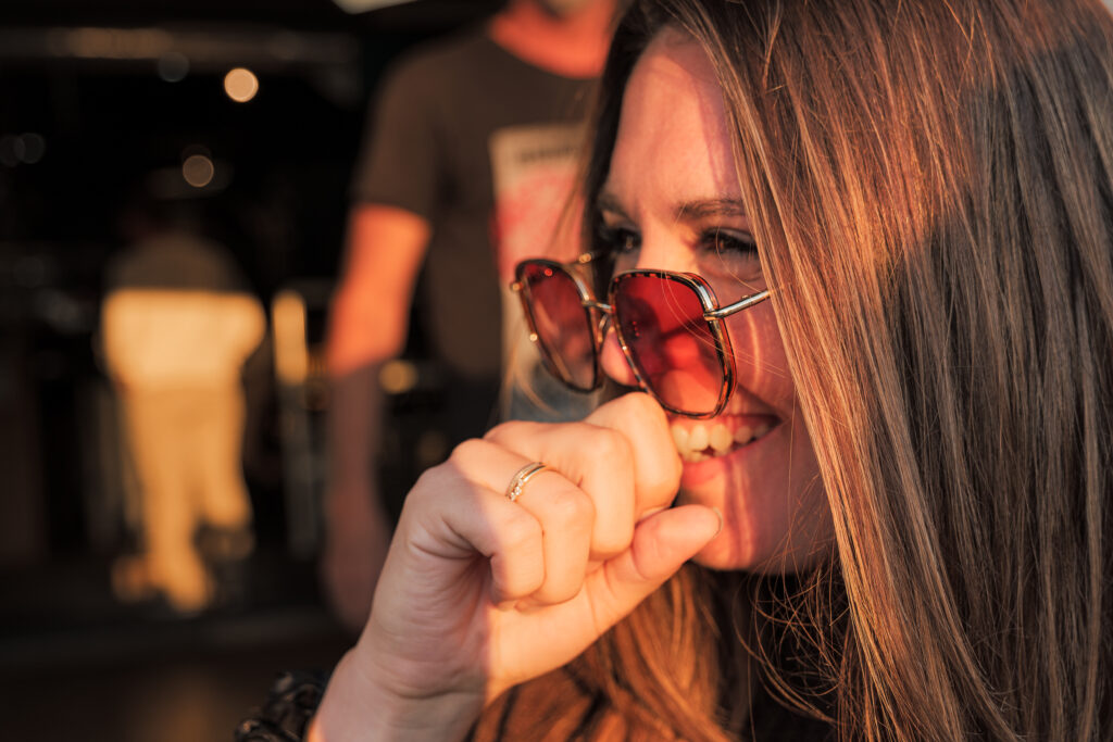 Jeune femme portant des lunettes de soleil en plan rapproché à la terrasse d'un café riant aux éclats dans la lumière du couché de soleil 