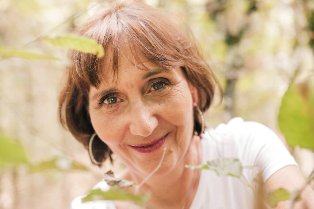 Portrait d'une femme d'âge moyen brune aux yeux noisettes, photographiée en Creuse avec un arrière plan et premier plan flou de verdure