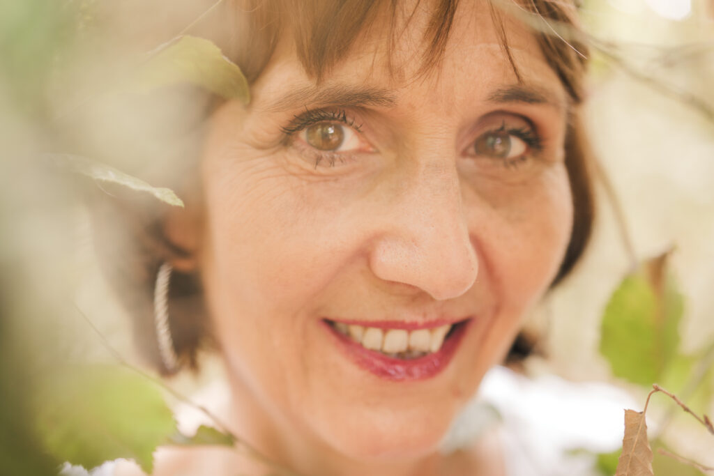Portrait d'une femme d'âge moyen brune aux yeux noisettes, photographiée en Creuse avec un arrière plan et premier plan flou de verdure