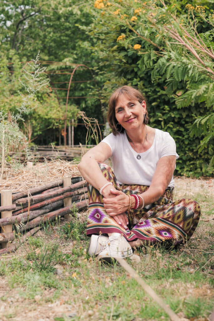 Portrait d'une femme d'âge moyen brune aux yeux noisettes, assise en tailleurs dans un jardin