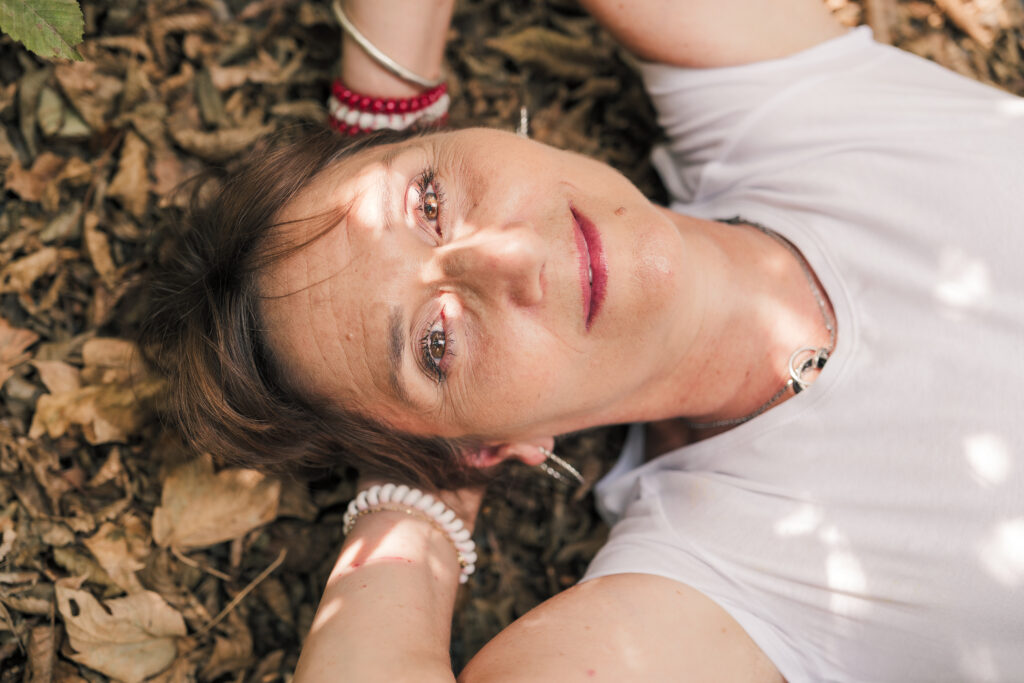Portrait rapproché d'une femme d'âge moyen brune aux yeux noisettes, allongée dans les feuilles morte, photographiée en Creuse