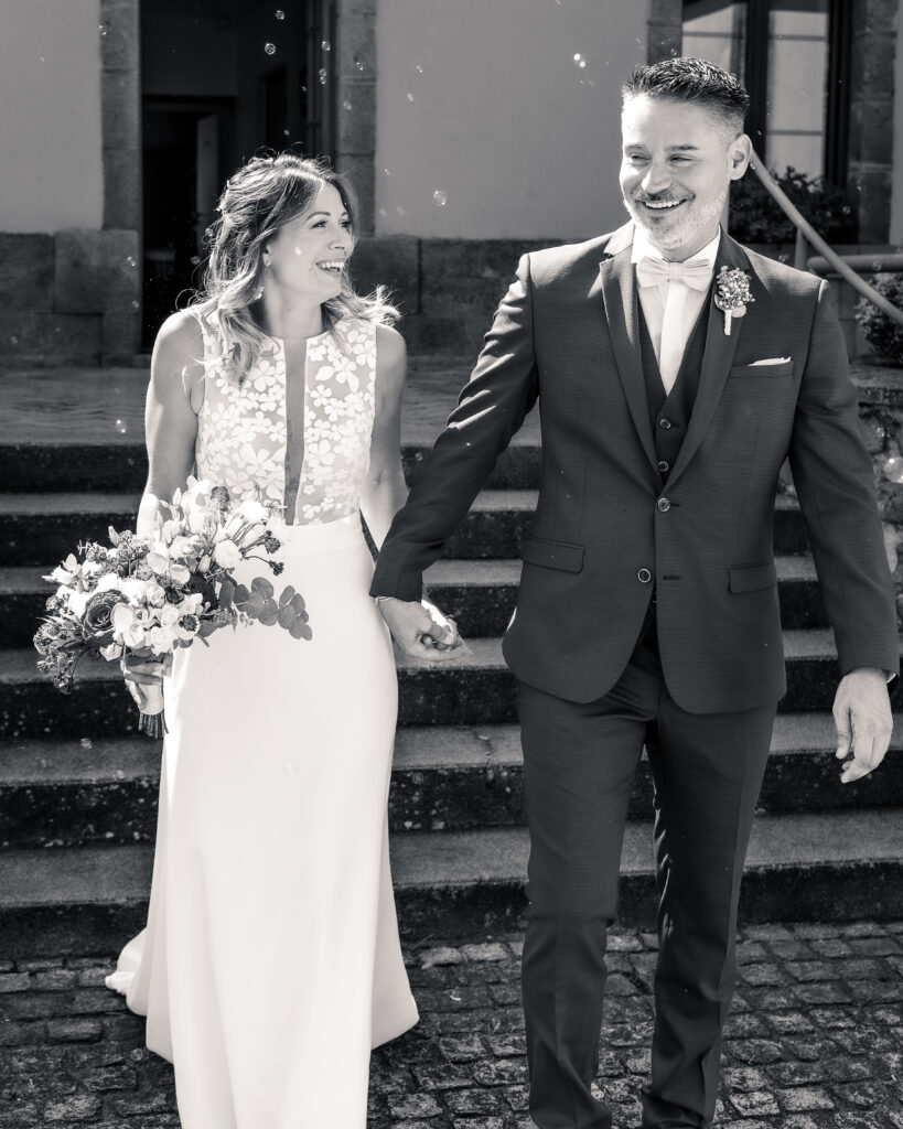 Portrait en pied et en noir et blanc d'un couple de jeune mariés sortant de la mairie en se tenant la main.