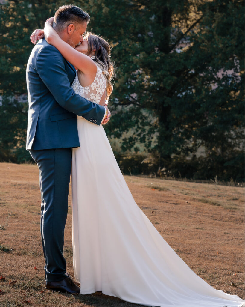 Portrait en pied de profil d'un couple de jeune mariés s'embrassant et enlacé au coucher du soleil au milieu d'un champ.