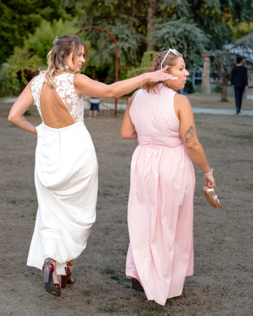 Portrait en pied de dos de la mariée et de sa témoin s'éloignant vers la salle de réception