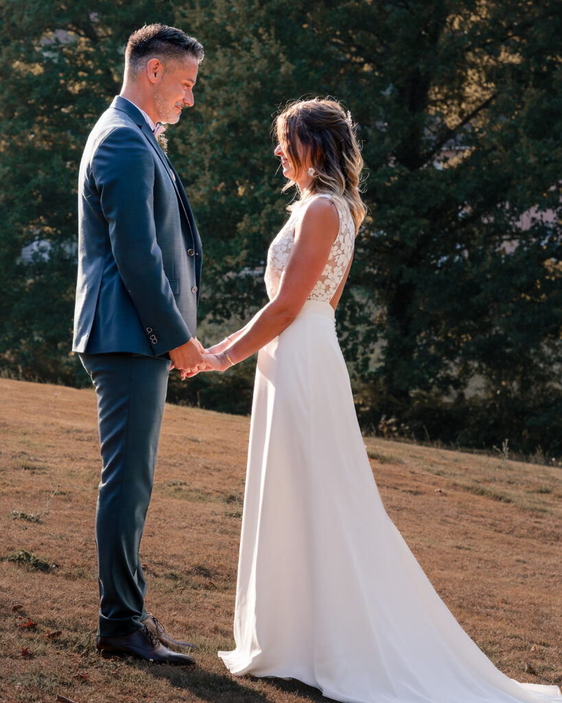 Portrait en pied de profil d'un couple de jeune mariés face à face se tenant les mains au coucher du soleil au milieu d'un champ.